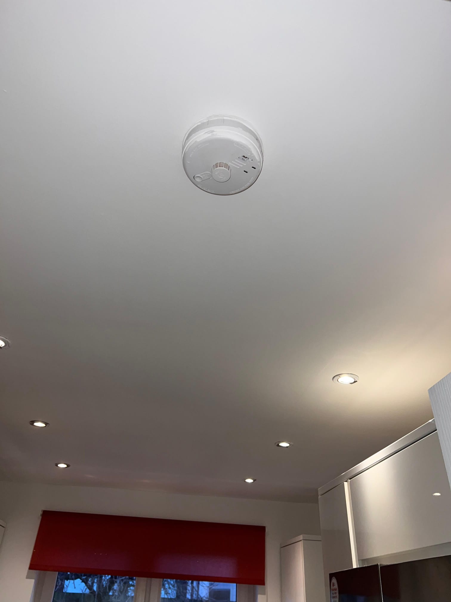 A moment in a room with a white ceiling from which a round white smoke detector is hanging